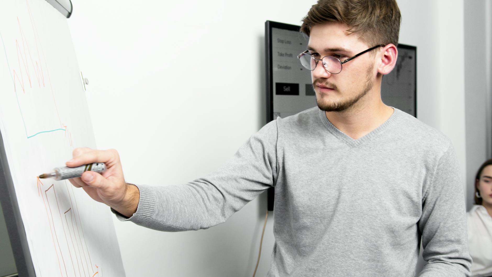 A Man Wearing Eyeglasses Writing on a Whiteboard