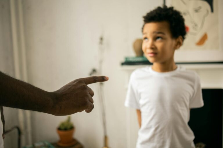 A father points and scolds his son indoors, emphasizing discipline.